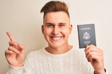 Amerika Birleşik Devletleri pasaportu taşıyan genç yakışıklı bir adam izole edilmiş beyaz bir arka plan üzerinde çok mutlu bir şekilde elini ve parmağını kenarı işaret ediyor.