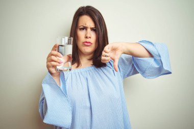 Young beautiful woman drinking a glass of fresh water over isolated background with angry face, negative sign showing dislike with thumbs down, rejection concept