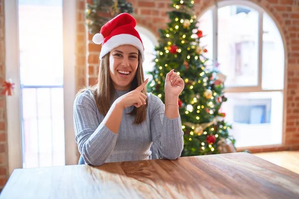 클로스 모자를 크리스마스 장식을 테이블에 미소를 손가락으로 가리키는 카메라를 바라보는 — 스톡 사진