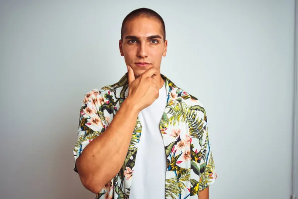 Young handsome man on holidays wearing Hawaiian shirt over white background looking confident at the camera with smile with crossed arms and hand raised on chin. Thinking positive.