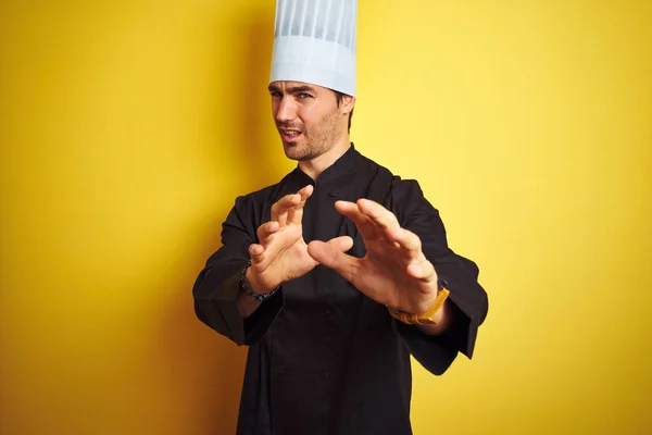 穿着制服和帽子站在孤立的黄色背景上的年轻厨师讨厌的表情 不高兴和害怕做厌恶的脸 因为厌恶的反应 举起手来 令人烦恼的概念 — 图库照片