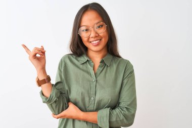 Yeşil gömlek ve gözlük takan genç Çinli bir kadın izole edilmiş beyaz arka planda, yüzünde kocaman bir gülümseme, eli ve parmağı kameraya bakıyor..