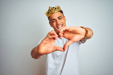 Kral tacı takan genç Brezilyalı adam izole edilmiş beyaz arka planda duruyor. Aşkla gülümsüyor. Elleriyle kalp sembolü ve şekli gösteriyor. Romantik konsept.