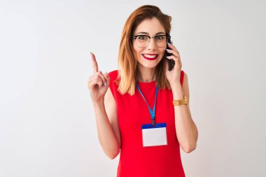 Kimlik kartı takan kızıl saçlı iş kadını izole edilmiş beyaz arka planda telefonla konuşuyor. Bir fikir ya da soru işareti ile şaşırmış, mutlu yüzle bir numara.