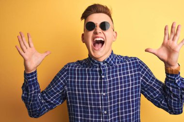 Sarı arka plan üzerinde gündelik gömlek ve güneş gözlüğü takan genç yakışıklı adam çılgın ve başarıyı kollarını kaldırıp heyecanla haykırarak kutluyor. Kazanan konsept