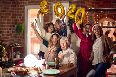 Mutlu ve kendinden emin gülümseyen güzel bir kadın grubu. Evde 2020 balon tutan noel ağacı etrafında poz vermek