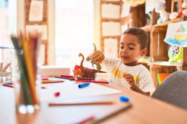 Güzel Afrikalı Amerikalı çocuk anaokulunda dinozor oyuncağıyla oynuyor.