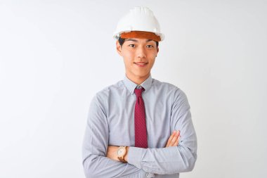 Kravat ve kask takan Çinli mimar, izole edilmiş beyaz arka plan üzerinde durup kollarını kavuşturup kameraya bakarken gülümsüyor. Pozitif kişi.