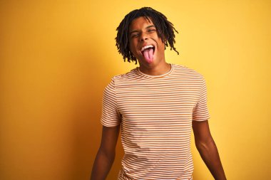 Sarı arka planda duran çizgili tişörtlü Afro adam mutlu bir ifadeyle dilini dışarı çıkarıyor. Duygu kavramı.