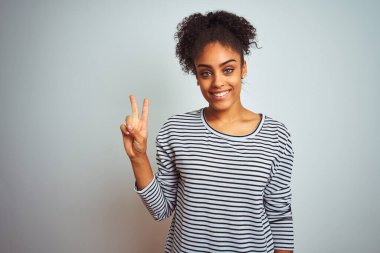 Siyah çizgili tişört giyen Afro-Amerikalı kadın izole edilmiş beyaz arka planda duruyor ve iki numarayı işaret ediyor..