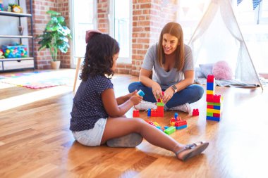 Güzel öğretmen ve küçük kız anaokulunda inşaat bloklarıyla oynuyorlar.