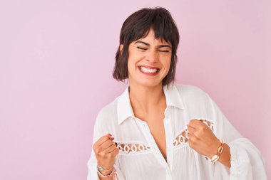 Yaz beyaz gömlek giyen genç güzel kadın izole pembe arka plan üzerinde duran başarı için heyecanlı kolları ile zafer gülümseyerek kutluyor kaldırdı. Kazanan kavramı.