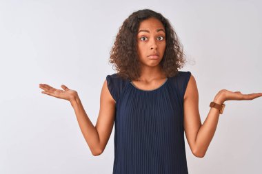 İzole edilmiş beyaz arka plan üzerinde duran mavi elbiseli genç Brezilyalı kadın elleri ve kolları havada, kafası karışmış bir ifade takınıyor. Şüphe kavramı.