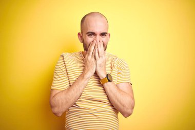 Sakallı, sarı renkli tişörtlü, sakallı genç bir adam gülerek ve utanarak kıkırdayarak elleri, dedikoduları ve skandal konseptini kullanıyor.