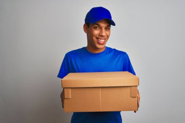Genç yakışıklı Arap teslimatçı elinde bir kutu, izole edilmiş beyaz arka planda duruyor. Mutlu bir yüzü var, gülümsüyor ve kendine güvenen bir gülümsemeyle dişlerini gösteriyor.