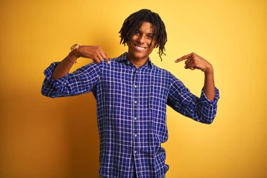Rastgele gömlek giyen Afro bir adam izole edilmiş sarı arka planda duruyor. Yüzünde bir gülümsemeyle, gururlu ve mutlu bir şekilde kendini işaret ediyor..