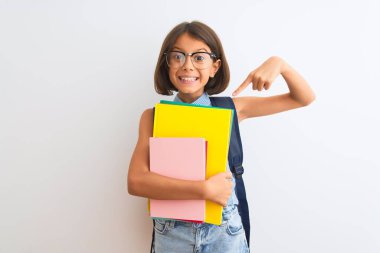 Güzel öğrenci kız, sırt çantası gözlüğü takıyor. İzole edilmiş beyaz arka plan üzerinde. El ve parmağıyla işaret ederek çok mutlu.