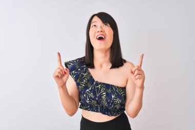 Yazlık çiçekli tişört giyen genç, güzel Çinli bir kadın izole edilmiş beyaz arka planda şaşkın şaşkın bakıyor, parmaklarıyla işaret ediyor ve kollarını kaldırıyordu..