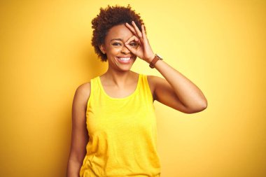 Beauitul Afro-Amerikalı kadın izole edilmiş sarı arka plan üzerinde yaz tişörtü giyiyor. El hareketleriyle gülümsüyor, gözleriyle mutlu yüzlere bakıyor..