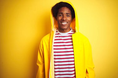 Kapüşonlu yağmurluk giyen Afrikalı bir adam izole edilmiş sarı arka planda mutlu ve havalı bir gülümsemeyle dikiliyor. Şanslı kişi..