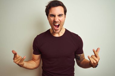 İzole edilmiş beyaz arka planda mor tişörtlü, dövmeli genç yakışıklı adam elleri havada rock sembolü yaparken çılgın bir ifadeyle bağırıyor. Müzik yıldızı. Ağır konsept.