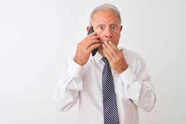 Üst düzey gri saçlı işadamı, akıllı telefondan izole edilmiş beyaz arka plan üzerinden konuşuyor. Ağzı, hata yüzünden utançla kaplı, korkunun ifadesi, sessizlikten korkmak, gizli bir konsept.