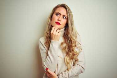 Kış balıkçı yaka kazak giyen güzel bir kadın izole edilmiş beyaz arka plan üzerinde elleri çenesinde soru sormayı düşünen düşünceli bir yüz ifadesi var. Düşünceli bir yüzle gülümsüyor. Şüphe kavramı.