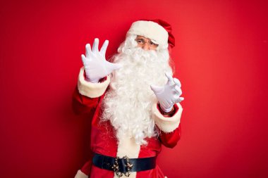 Noel Baba kostümü giymiş orta yaşlı yakışıklı bir adam izole edilmiş kırmızı arka plan üzerinde korkmuş ve korkudan dehşete düşmüş halde duruyor. El hareketlerini durdur, şok içinde bağır. Panik konsepti.