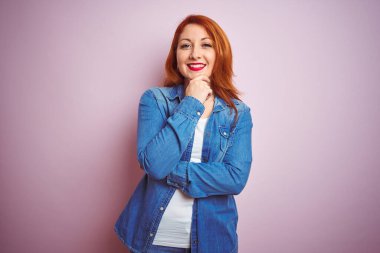 İzole edilmiş pembe arka plan üzerinde duran güzel, kızıl saçlı kadın kameraya kollarını kavuşturmuş ve çenesini kaldırmış şekilde gülümsüyor. Olumlu düşünüyorum..