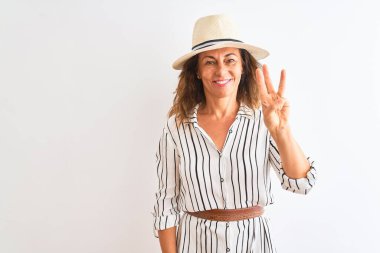 Orta yaşlı iş kadını çizgili elbise ve şapkalı, izole edilmiş beyaz arka planda üç numaralı parmaklarıyla gülümseyerek kendinden emin ve mutlu bir şekilde görünüyor..
