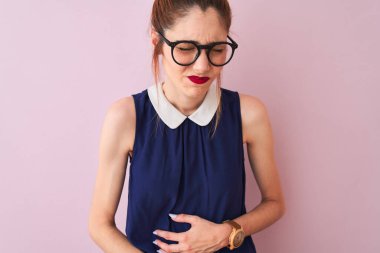 Saçlı, at kuyruklu, zarif bir elbise ve gözlük takan kızıl saçlı kadın, midesi bulanan, acı verici bir hastalık yüzünden izole edilmiş pembe arka planda. Ache kavramı.