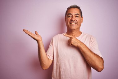 İzole edilmiş pembe arka plan üzerinde duran yakışıklı orta yaşlı adam kameraya hayret ediyor ve gülümsüyor..