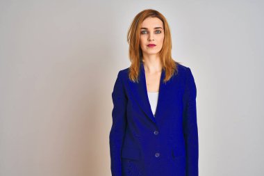 Kızıl saçlı beyaz iş kadını izole edilmiş arka planda takım elbise giyiyor ve yüzünde ciddi bir ifade var. Basit ve doğal bir şekilde kameraya bakıyorsun..