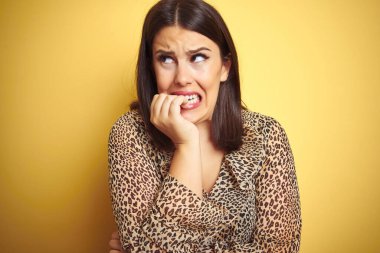 Sarıya boyanmış arka planda leopar desenli gömlek giyen genç, güzel esmer kadın elleri ağız yiyen tırnaklarıyla gergin ve stresli görünüyor. Endişe sorunu.