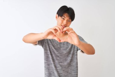 Sıradan tişörtler giyen genç Çinli bir adam izole edilmiş beyaz arka planda duruyor. Aşkla gülümsüyor ve elleriyle kalp sembolü ve şekli gösteriyor. Romantik konsept.