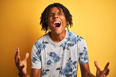 Rastalı tişörtlü Afro bir adam izole edilmiş sarı arka planda çılgın deli bağırıyor ve agresif bir ifade ve kolla bağırıyor. Hayal kırıklığı konsepti.