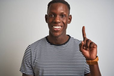 Siyah çizgili tişört giyen Afro-Amerikalı bir adam izole edilmiş beyaz arka planda duruyor. Bir fikir ya da soru işareti ile şaşırmış, mutlu yüzle bir numarayı işaret ediyor.