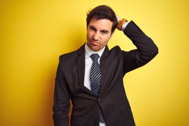 Takım elbiseli ve kravatlı genç yakışıklı işadamı izole edilmiş sarı arka planda dikiliyor ve soru soruyor. Şüpheyle kararsız, kafa kafaya düşünerek. Düşünceli kavram.