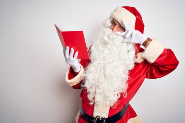 Orta yaşlı bir adam Noel Baba kostümü giyip izole edilmiş beyaz arka planda kitap okuyor. Yüzünde parmaklarıyla barış sembolü yapıyor.