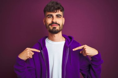 Dövme ile genç adam izole sarı arka plan üzerinde yüz gülümseme ile kendine güvenen görünümlü üzerinde çizgili polo ayakta giymiş, parmaklarıyla gurur ve mutlu kendini işaret.