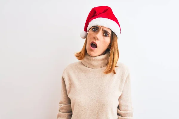 漂亮的红头发女人 头戴圣诞帽 背景孤寂 脸上带着震惊的表情 脸上带着怀疑和讽刺的表情 张大了嘴 吃惊极了 — 图库照片