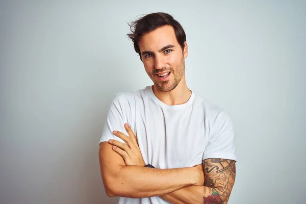 Young handsome man with tattoo wearing casual t-shirt over isolated white background happy face smiling with crossed arms looking at the camera. Positive person.