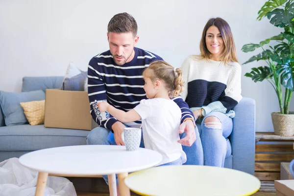 美しい家族 ソファに座ってコーヒーを飲む両親は 彼の子供が段ボール箱の周りに新しい家で遊んでいるのを見て — ストック写真