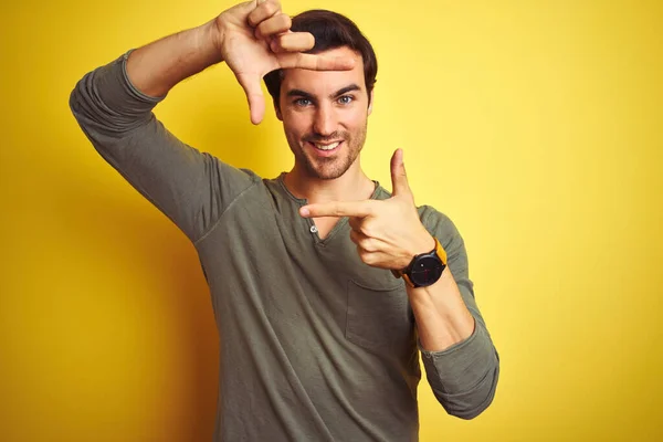 年轻英俊的男子穿着休闲的T恤 站在孤立的黄色背景上 微笑着 用双手和手指制作出笑脸的框架 创意和摄影概念 — 图库照片