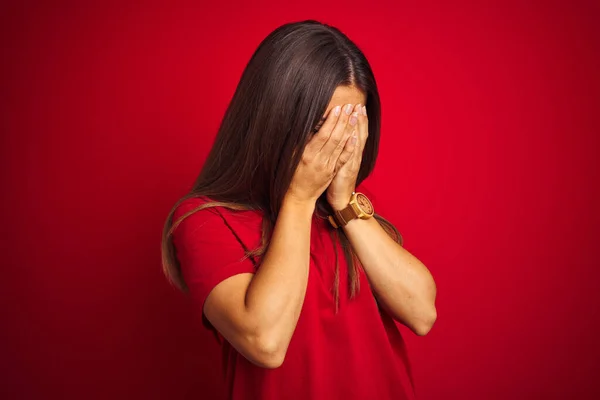 泣きながら手で顔を覆う悲しい表情で孤立した赤い背景の上にTシャツを着た若い美しい女性 うつ病の概念 — ストック写真