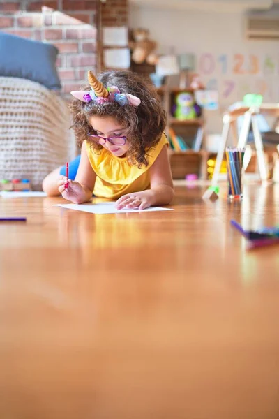 아름다운 아기가 안경을 유니콘 왕관을 유치원에서 종이와 연필을 사용하여 바닥에 — 스톡 사진