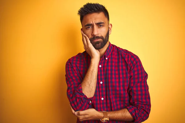Young indian man wearing casual shirt standing over isolated yellow background thinking looking tired and bored with depression problems with crossed arms.
