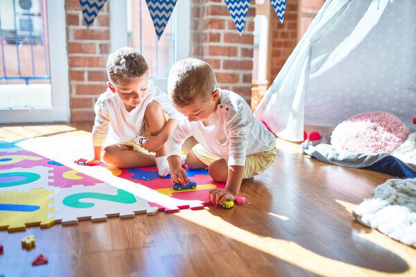 Очаровательные блондинки-близнецы играют с машинами вокруг кучи игрушек в детском саду
