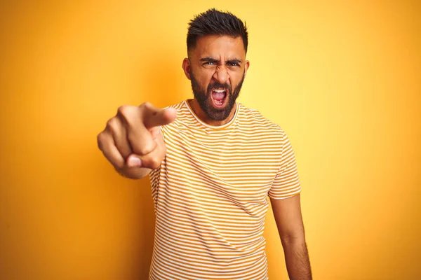 若いインド人の男を着てTシャツの上に立って孤立した黄色の背景を指して不満とカメラに不満 怒っていると激怒あなたと一緒に — ストック写真