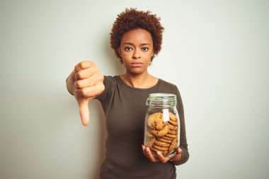 Afrika kökenli Amerikalı bir kadın, izole edilmiş arka planda çikolatalı kurabiye kavanozunu tutuyor. Kızgın bir yüzü var.
